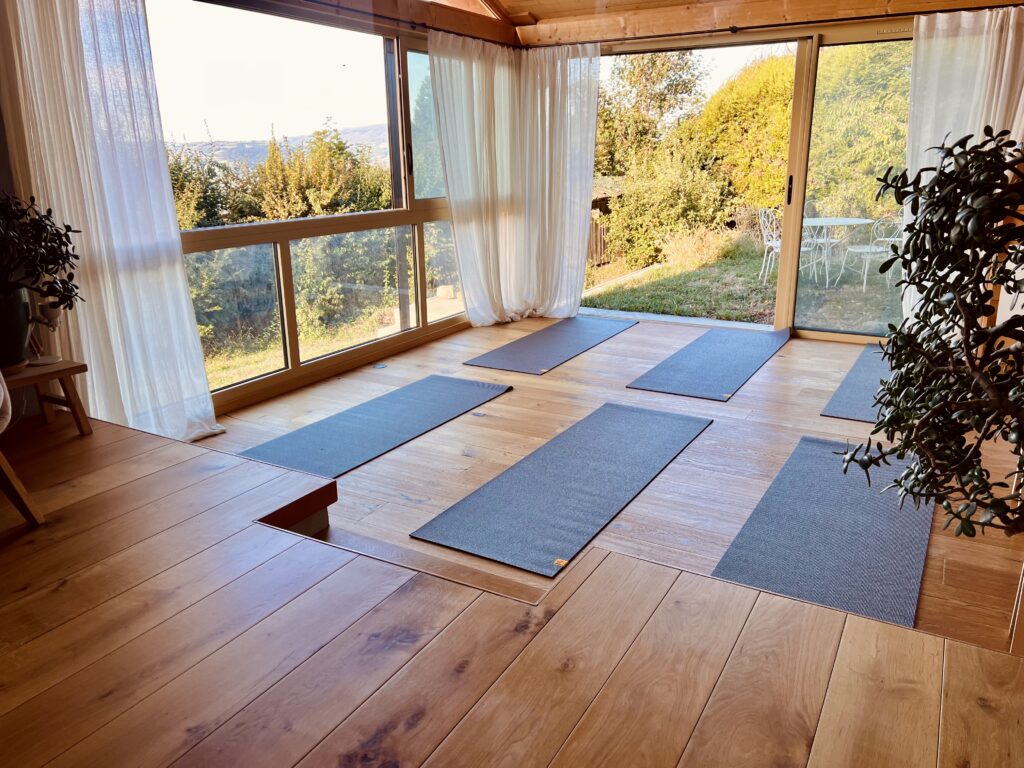 salle de yoga doux au Sanctuaire à Fillinges, avec tapis installés face aux grandes baies vitrées donnant sur la végétation